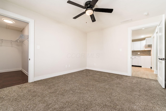 unfurnished bedroom with baseboards, carpet floors, ceiling fan, a closet, and a walk in closet