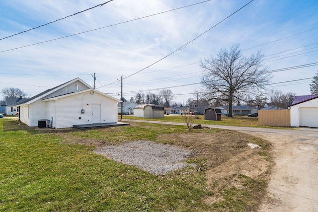 view of yard featuring fence, dirt driveway, central AC, a storage shed, and an outdoor structure