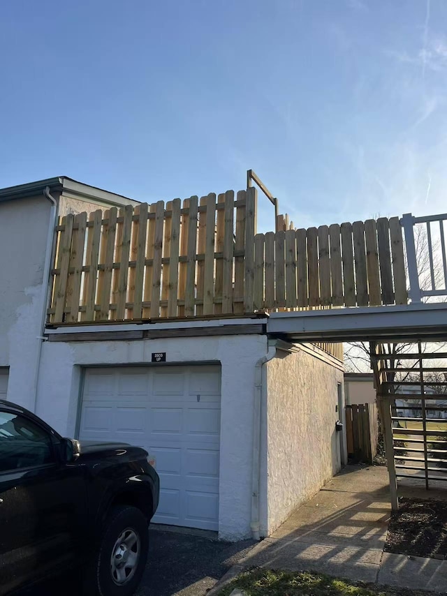 view of side of home with stucco siding, a garage, and fence