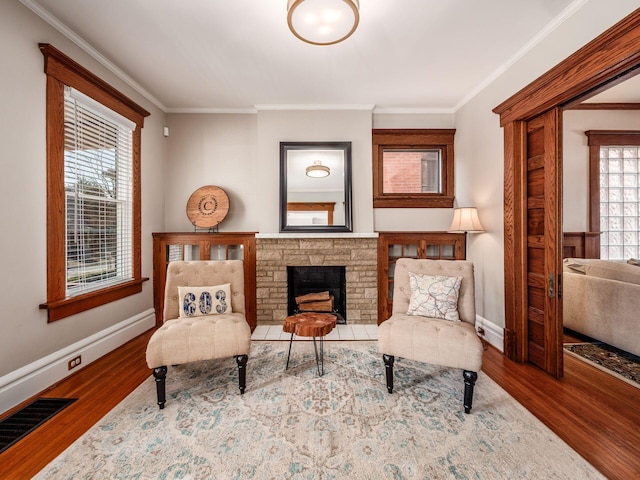 living area featuring a stone fireplace, crown molding, wood finished floors, and visible vents