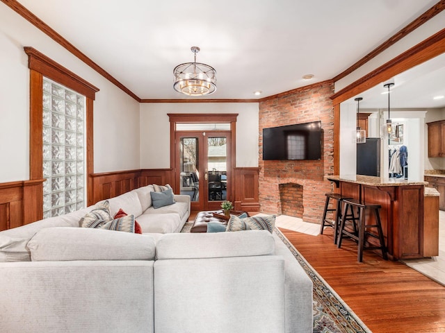 living room with wainscoting, a brick fireplace, an inviting chandelier, and light wood-style floors