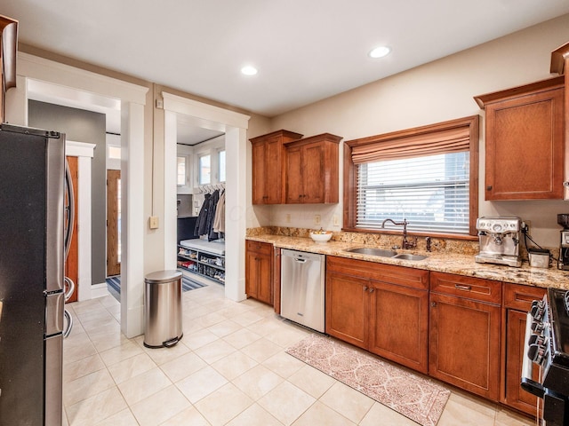 kitchen featuring light stone counters, appliances with stainless steel finishes, brown cabinetry, and a sink