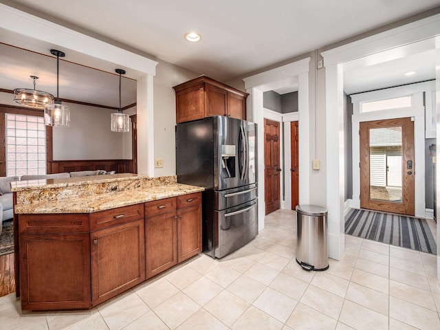 kitchen with brown cabinetry, light stone counters, a peninsula, stainless steel refrigerator with ice dispenser, and hanging light fixtures