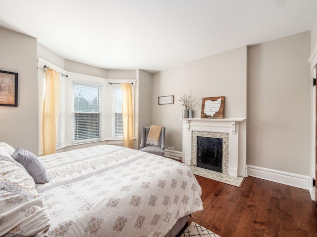 bedroom with dark wood finished floors, a fireplace with flush hearth, and baseboards