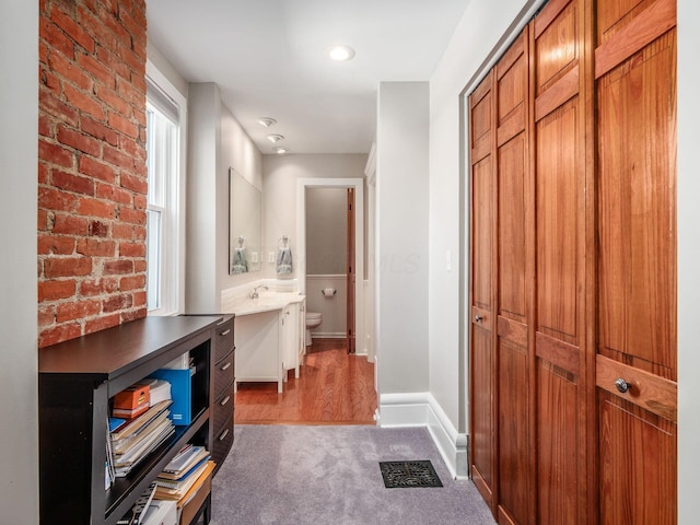 corridor featuring carpet, visible vents, baseboards, brick wall, and a sink