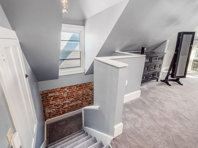 stairway featuring carpet flooring, brick wall, baseboards, and lofted ceiling