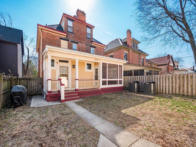 rear view of house featuring cooling unit, covered porch, a chimney, fence private yard, and brick siding