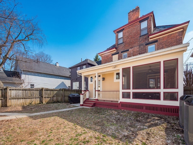 view of front of home featuring a sunroom, brick siding, central AC unit, fence private yard, and a chimney