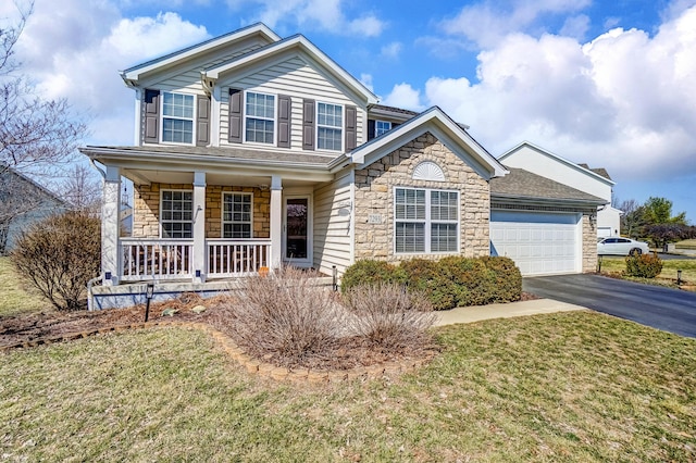 traditional home with aphalt driveway, a porch, a front yard, stone siding, and an attached garage