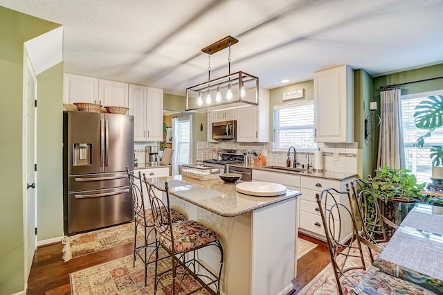 kitchen with a sink, a kitchen island, stainless steel appliances, white cabinets, and decorative backsplash