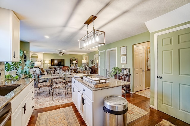 kitchen featuring light stone countertops, dark wood finished floors, open floor plan, white cabinets, and a ceiling fan