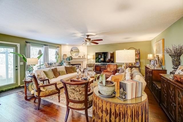 living room featuring a fireplace, dark wood-type flooring, and a ceiling fan