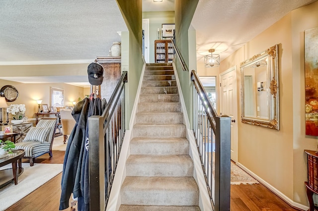 stairway with a healthy amount of sunlight, a textured ceiling, baseboards, and wood finished floors