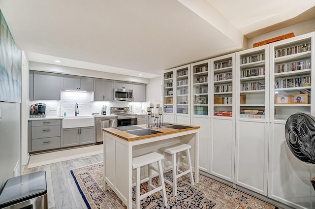 kitchen with light wood-style flooring, a sink, stainless steel appliances, gray cabinetry, and backsplash