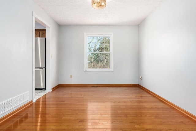 unfurnished room with visible vents, baseboards, light wood-style floors, and a textured ceiling