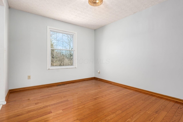 empty room featuring baseboards, visible vents, light wood-type flooring, and a textured ceiling