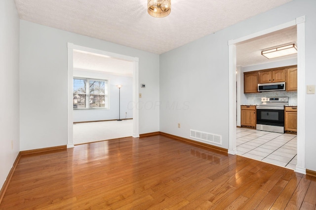 unfurnished living room with light wood finished floors, visible vents, a textured ceiling, and baseboards