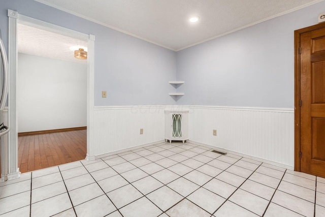 spare room featuring a textured ceiling, ornamental molding, visible vents, and wainscoting