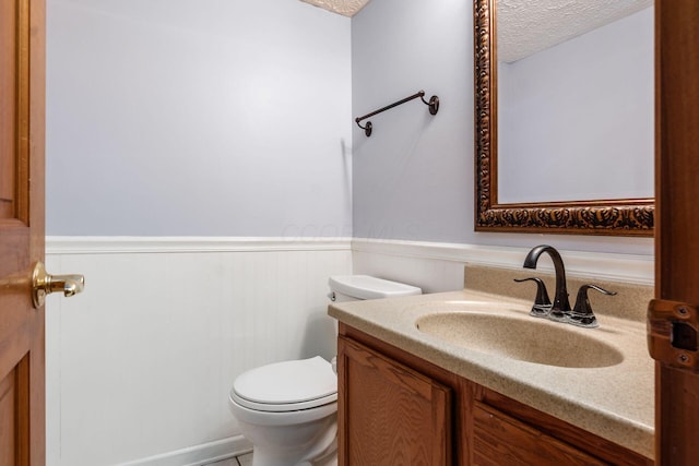 bathroom with a textured ceiling, toilet, vanity, and wainscoting