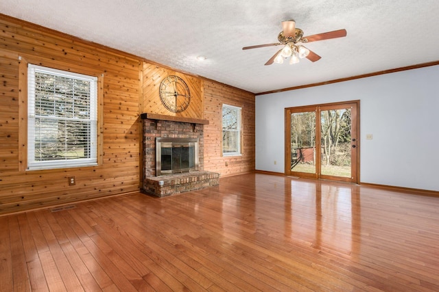 unfurnished living room with baseboards, wood walls, hardwood / wood-style flooring, a textured ceiling, and a ceiling fan