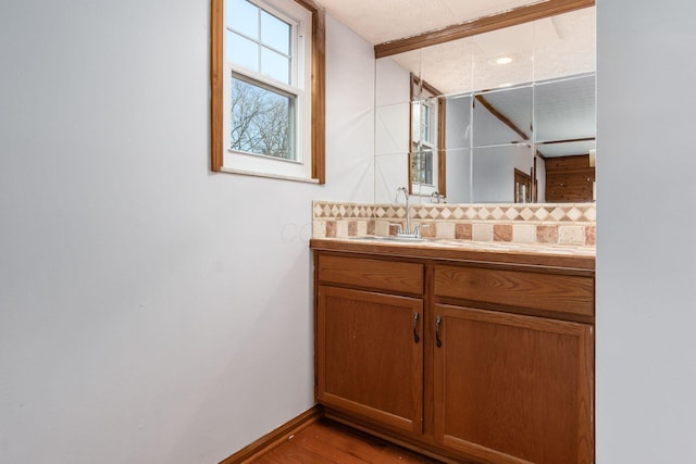 bathroom with baseboards, tasteful backsplash, wood finished floors, and vanity