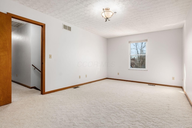 carpeted empty room featuring visible vents, a textured ceiling, and baseboards