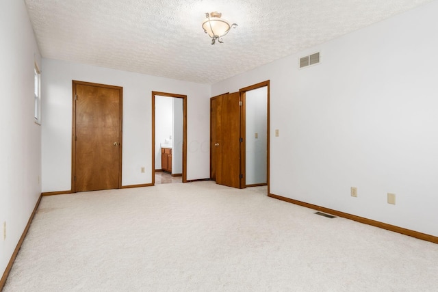 unfurnished bedroom with a textured ceiling, light colored carpet, visible vents, and baseboards