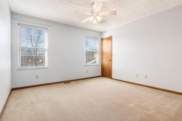 empty room with light carpet, ceiling fan, a textured ceiling, and baseboards