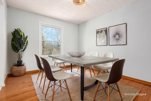 dining area featuring baseboards, light wood-type flooring, and a textured ceiling