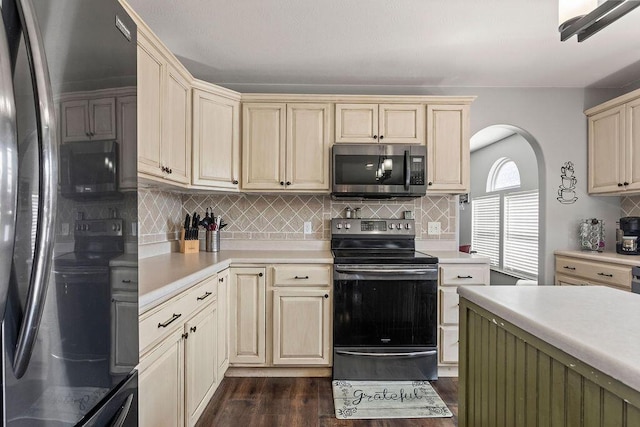 kitchen with light countertops, decorative backsplash, appliances with stainless steel finishes, cream cabinets, and dark wood-style floors