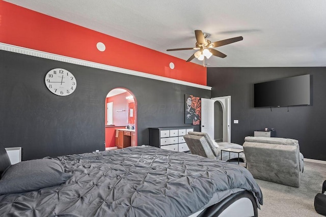 carpeted bedroom with a ceiling fan, baseboards, lofted ceiling, arched walkways, and ensuite bathroom