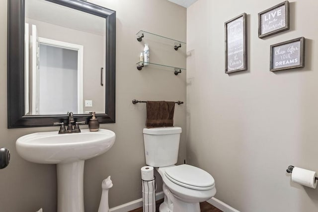 half bath featuring toilet, baseboards, and a sink