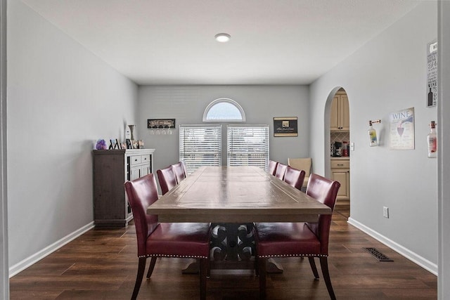 dining space featuring arched walkways, dark wood-type flooring, and baseboards