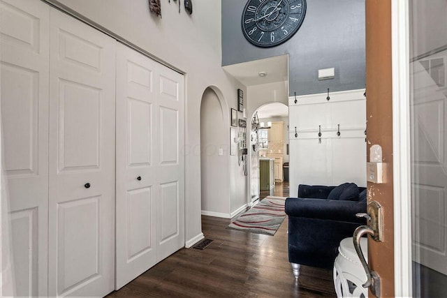 hallway with baseboards, arched walkways, and dark wood-style floors