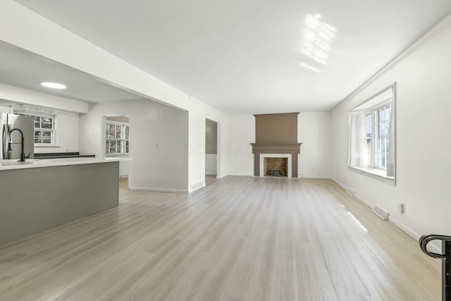 unfurnished living room with visible vents, baseboards, a fireplace with flush hearth, a sink, and light wood-type flooring