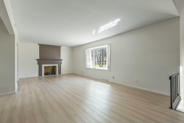 unfurnished living room with light wood finished floors, a fireplace with flush hearth, baseboards, and visible vents