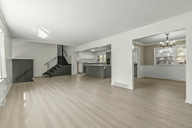 unfurnished living room featuring light wood finished floors, visible vents, stairway, a notable chandelier, and a sink