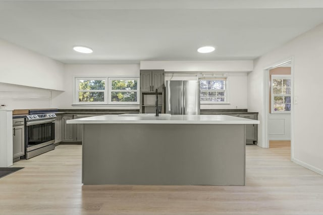 kitchen with a sink, gray cabinetry, light wood-type flooring, and stainless steel appliances