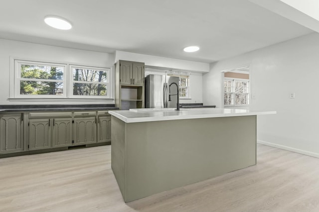 kitchen featuring an island with sink, baseboards, freestanding refrigerator, and light wood-style floors