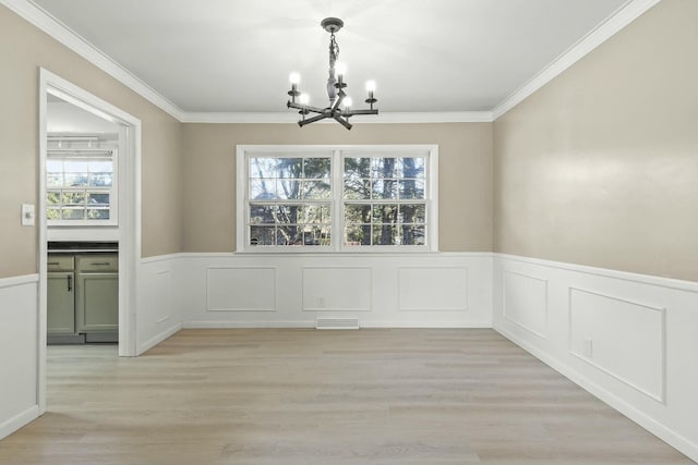 unfurnished dining area with a wainscoted wall, visible vents, ornamental molding, light wood-style floors, and a chandelier