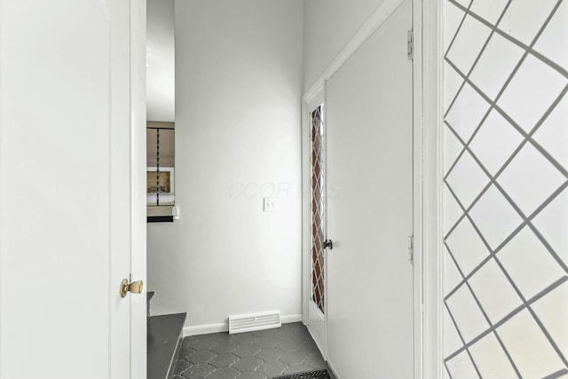 corridor featuring visible vents, baseboards, and dark tile patterned floors