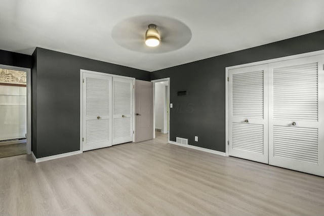 unfurnished bedroom featuring light wood-style floors, visible vents, multiple closets, and baseboards