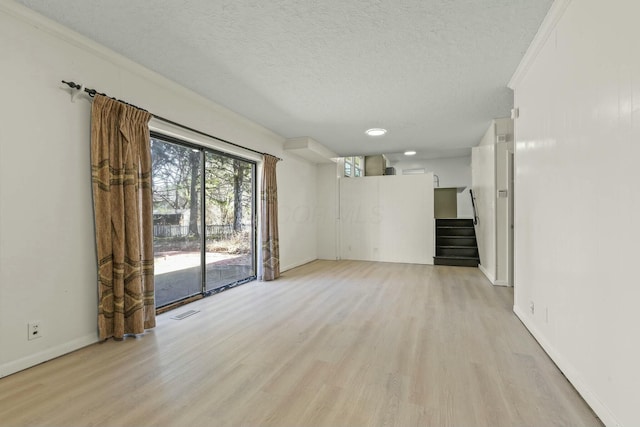 spare room with light wood-style flooring, a textured ceiling, stairs, and baseboards