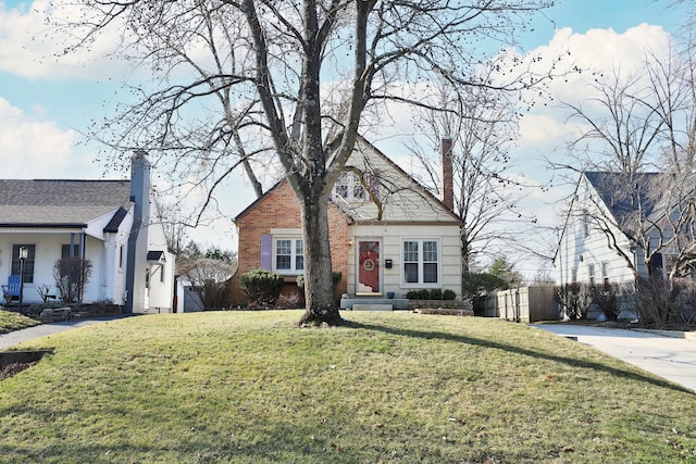 view of front of house with brick siding, a chimney, a front lawn, and fence