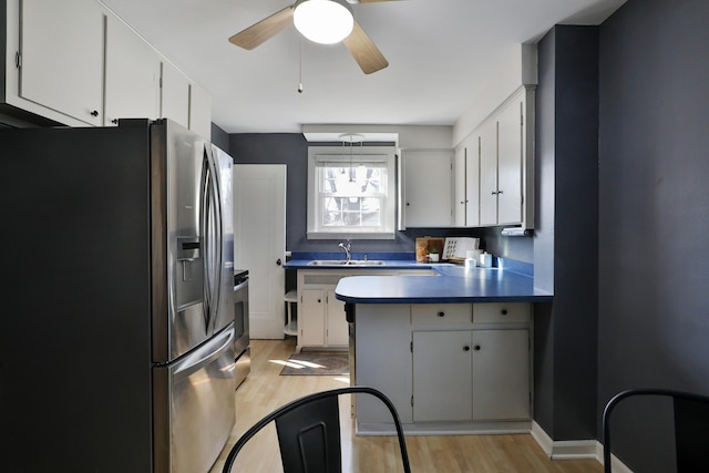 kitchen featuring a peninsula, a sink, stainless steel fridge, dark countertops, and light wood-type flooring