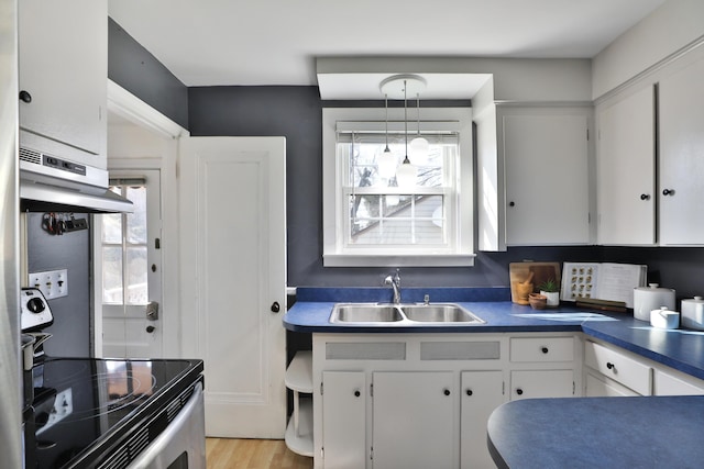 kitchen with dark countertops, under cabinet range hood, stainless steel electric range, white cabinetry, and a sink