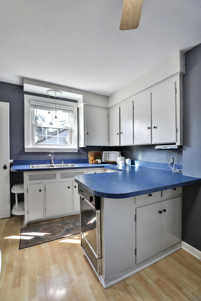 kitchen featuring a sink, light wood-type flooring, dark countertops, and a peninsula