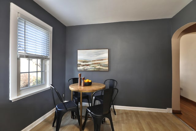 dining space with wood finished floors, baseboards, and arched walkways