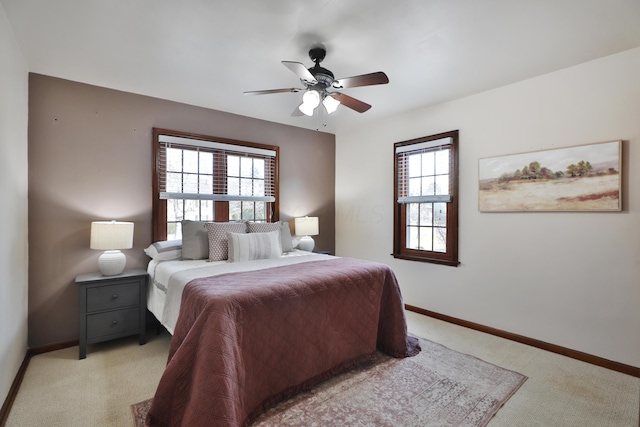 bedroom featuring baseboards, multiple windows, light colored carpet, and a ceiling fan