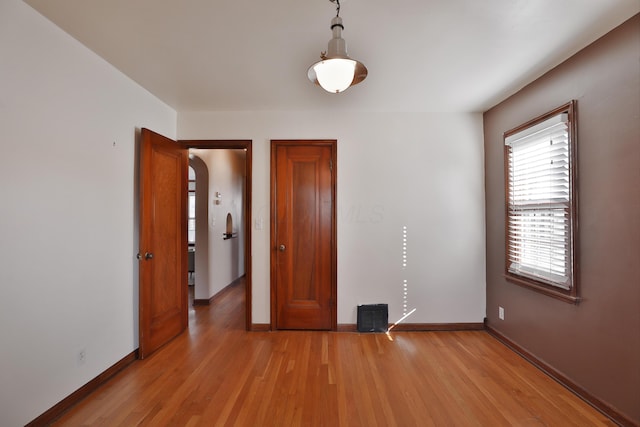 unfurnished bedroom featuring arched walkways, light wood-style flooring, and baseboards